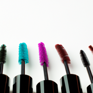 A close-up of a selection of brightly-colored mascaras in an array of shades, set against a plain white background.