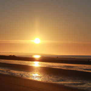 A bright and warm sun setting behind a golden beach.