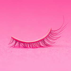 A close-up of a curled eyelash against a vibrant pink background.