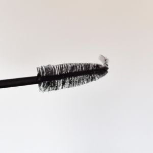 A close-up of a mascara wand with the tip of the bristles lightly brushing a wispy lash.