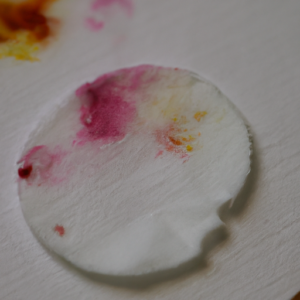 A closeup of a white cotton pad with splotches of colored makeup on it.