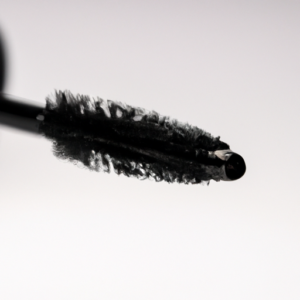 A close-up of a black mascara wand with a drop of mascara on the tip.