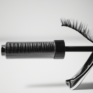 A black and white close-up photo of a single mascara wand with curled lashes.