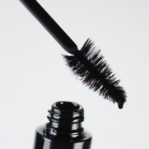 A closeup image of a mascara brush being dipped into a tube of mascara.